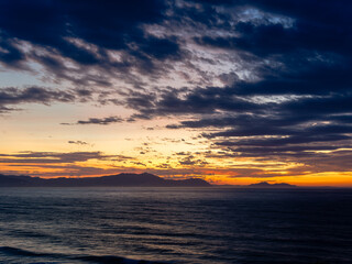 Ocean sunset with dramatic clouds over mountains © Paul