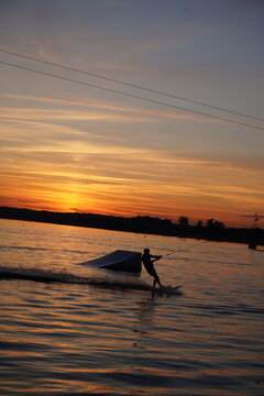 Silhouette of a wakeboarder riding on the water at golden sunset