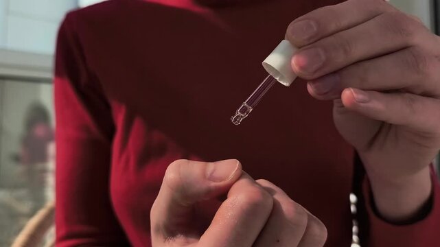 Hand applies liquid serum with dropper in close up. Careful dosing continues over skin during a personal beauty routine. Skincare treatment for wellness, spa, and cosmetic use..