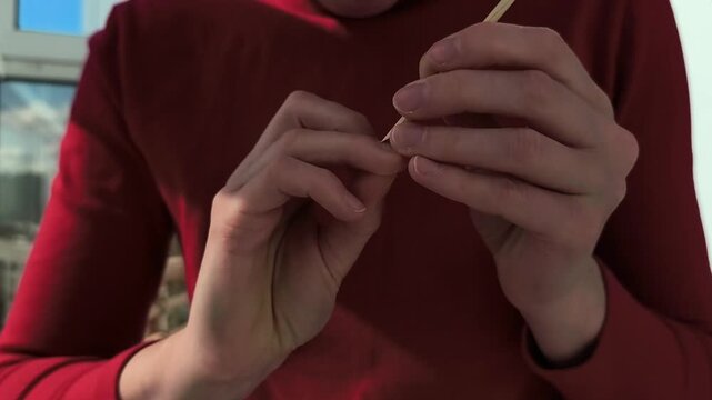 Hands clean a fingernail with a wooden cuticle stick in close up. Careful manicure motion continues indoors with natural light. Personal grooming and nail care routine..