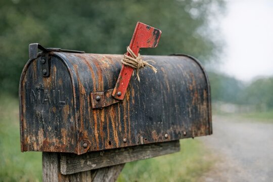 An old metal mailbox with a rusted surface and a distinctive red handle