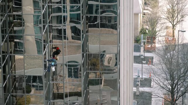 Professional abseiler carefully executing routine maintenance on skyscraper exterior amidst cityscape