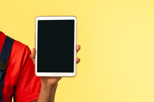 Friendly worker wearing blue uniform showing tablet with blank display with space for advertisement, pointing to camera, choosing you for order. Indoor studio shot isolated on yellow background.