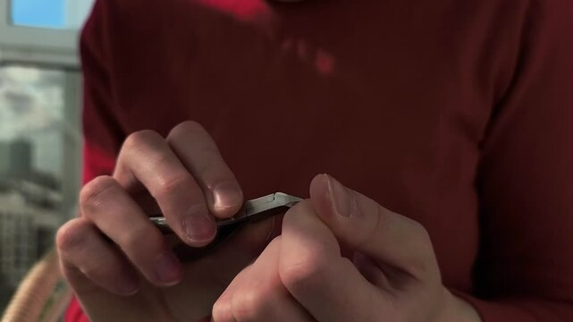 Hands trim a fingernail with a clipper near a window. The motion continues as the nail is shaped in close up indoor light. Personal care, grooming, and hygiene content for lifestyle use..