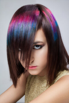 Mysterious lady colorful hair fringe covering eye staring camera bold makeup expressive look wearing gold shiny outfit posing isolated over gray background