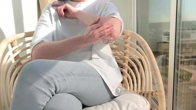 Woman applies cream on dry elbow skin moisturizing rough area at home. Female performs skincare routine improving hydration and comfort. Beauty concept highlights selfcare and wellness
