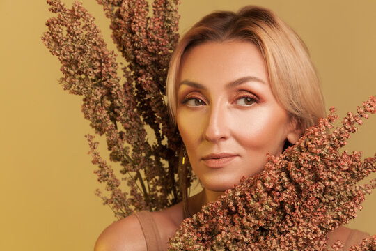 Confident blonde woman posing with autumn dried flowers looking aside posing isolated yellow studio background