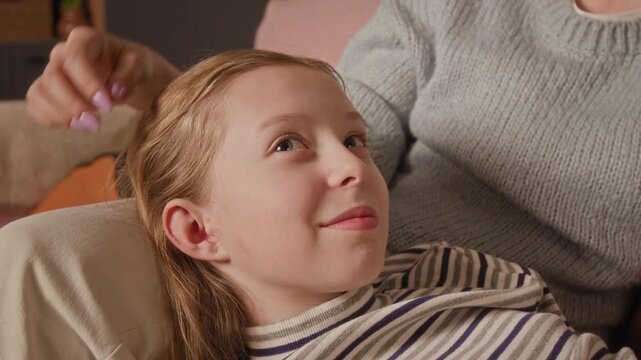 Close up of happy preteen girl sharing emotions with mother during trusting conversation while lying on parents lap in living room