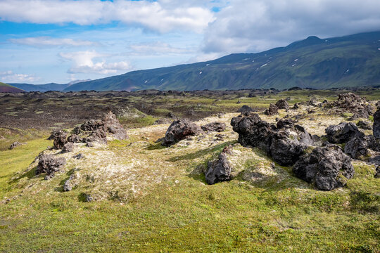Scenic view of rugged volcanic landscape in iceland with large rocks and green moss under a cloudy blue sky, capturing the natural beauty and unique geology of the region. Basalt rock