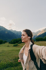 Naklejka premium A woman in a light jacket explores a green valley with mountains in the background, conveying an active outdoor lifestyle moment and scenic tranquility.