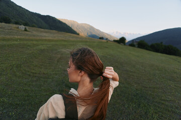 Naklejka premium Young woman outdoors in an open field ties her hair back, enjoying a peaceful moment as a gentle breeze moves across the grass.