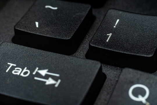 Close-up macro of black keyboard keys Tab and number 1 with white lettering, dramatic lighting on textured plastic surface. Technology concept.
