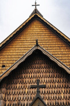 Traditional Norwegian stave church surrounded by spring countryside and forested hills under dramatic cloudy sky in Telemark, Norway. Dark wooden medieval-style architecture. 