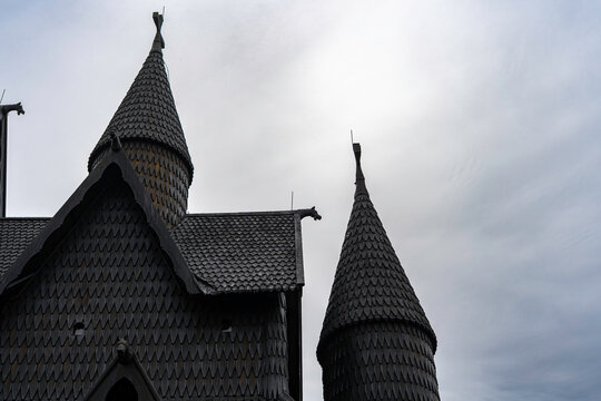 Traditional Norwegian stave church surrounded by spring countryside and forested hills under dramatic cloudy sky in Telemark, Norway. Dark wooden medieval-style architecture. 