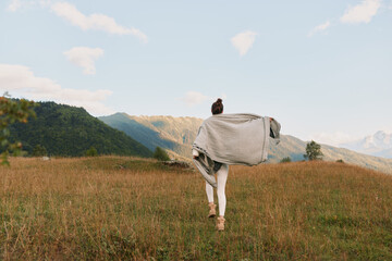 Naklejka premium Woman running through a sunlit field with a flowing shawl, open landscape, outdoor lifestyle, freedom and exploration, bright sky, distant hills, calm mood, natural light, candid moment.