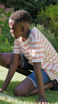 Vertical video: Noticing metal rod, teen kneeling aligning rod in backyard wearing red striped tee