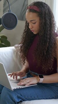 Vertical video: Placing laptop, woman on couch typing, speaking to mic, prepping show, maroon top