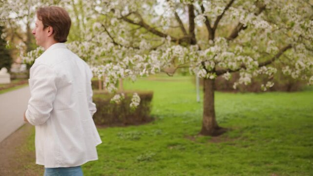 Man experiences hay fever and sneezing during allergy season in a lush park. 4K footage captures the reaction to pollen and spring blooms, including itchy eyes. High quality 