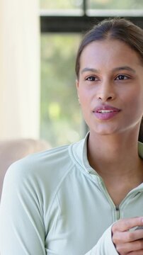 Vertical video: Glancing off-camera, woman in mint athletic top speaking, tapping tablet by window