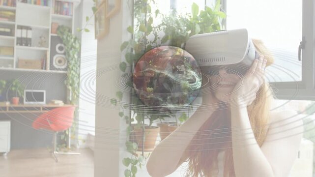 Woman putting on VR headset at home, summoning animated globe with orbits and manipulating for tech