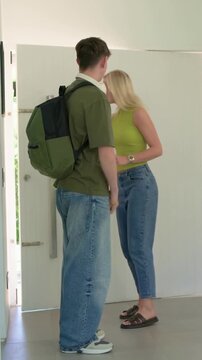 Vertical video: Door opening son entering home with backpack, mom lime top helping, dad hugging