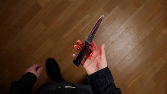 Person's hand covered in fresh blood, tightly gripping a kitchen knife with blood also dripping on its blade, suggesting violence, a crime scene, or a serious injury