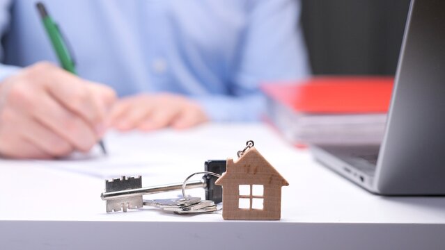 Person making a decision and signing an agreement for purchasing property, with home keys and a house keychain representing new ownership on the desk beside a laptop