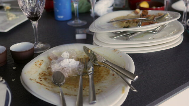 Stack of dirty dishes and glasses on dining table after festive meal, remains of food and used cutlery reflecting family holiday gathering and celebration at home