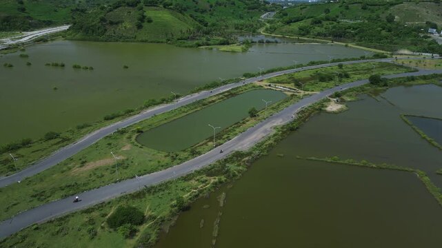 Aerial Coastal Road Over Saltpan Embankments And Pond Networks, Causeway Curves Through Wetland Basin, Remote Corridor For Transport And Local Access, Seasonal Water Patterns And Levees Visible
