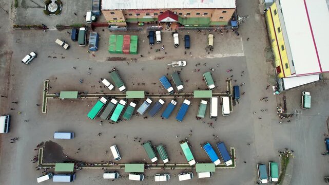 Aerial view of a bustling bus station featuring rows of colorful minibuses and people walking between platforms near urban buildings Wewak, East Sepik Province, Papua New Guinea.