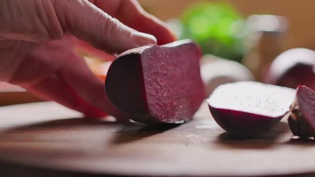 A knife slices along a beetroot on a wooden cutting board. Preparing fresh vegetables for a colorful roasted Sunday roast. Simple home cooking with wholesome ingredients