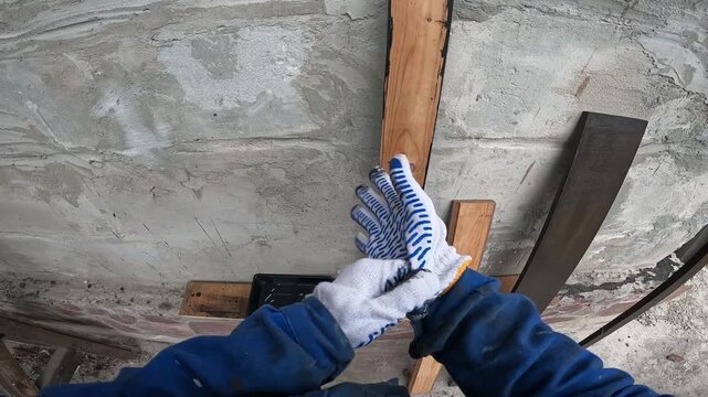 The process of painting wood. A builder paints a wooden beam black. A worker in a blue uniform and protective gloves applies paint with a brush. First-person view (POV). Redesign, handmade