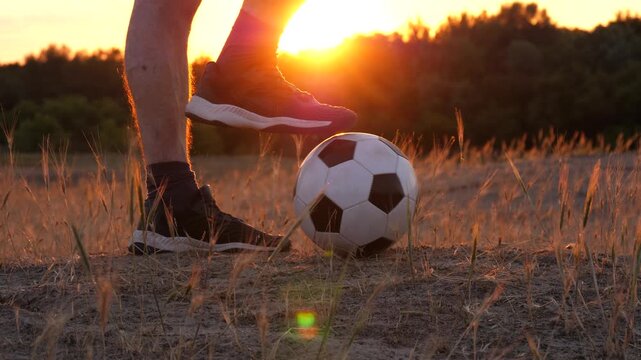 Close-up of foot on soccer ball at sunset in rural field. Casual play in countryside with warm golden light. Simple outdoor moment showing passion for football and active lifestyle. Football and