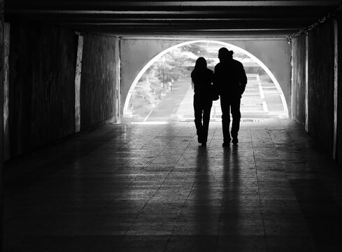 Tourist couple walking on underground pavement passage under land Silhouettes of two people in a tunnel. light coming from behind. Couple walking away from the camera. Lens facing against the light.