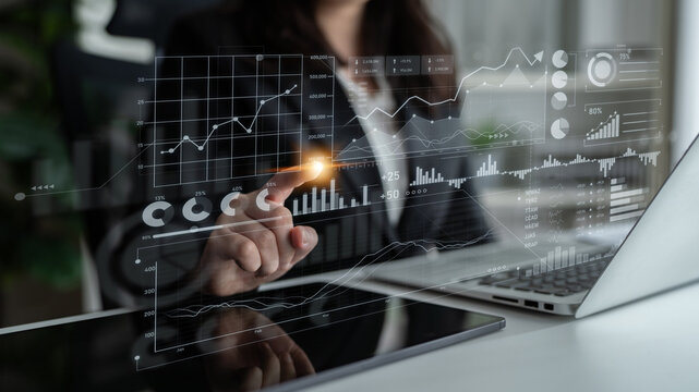 Business professional engages with interactive digital analytics while analyzing financial data on a laptop in a contemporary office, highlighting modern technology in workspaces. Scalp