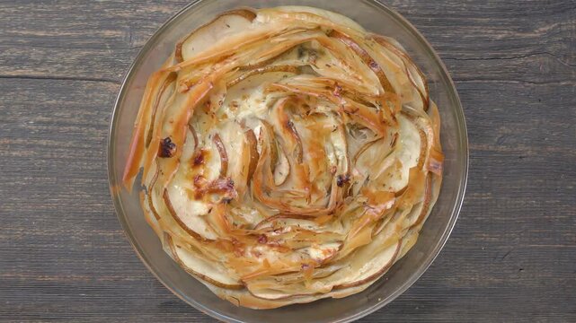 Top view of hands placing a fresh phyllo dough pie with pears and mix of cheeses on a wooden table. Homemade pastry in a transparent glass baking dish
