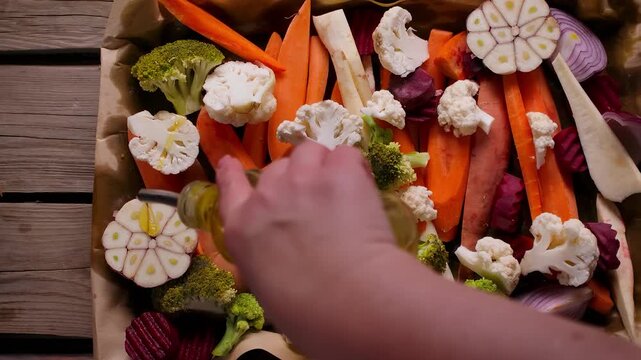 Woman pouring olive oil on tray of sliced vegetables like beets carrots and parsnip. Panning top view of preparation for healthy Sunday roast dinner