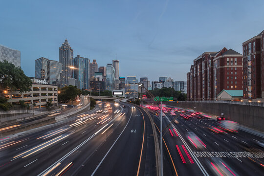 View of the Downtown Atlanta Skyline Cityscape showing several prominent buildings, highways, cars, and hotels on a beautiful clear evening after sunset as seen from a city street.