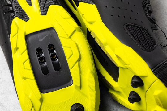 Yellow soles of brand new SPD cycling shoes on gray background. Mountain bike cycling shoes shot with flash light.