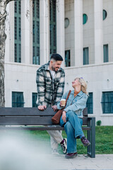 Young couple laughing and enjoying coffee on a city bench, sharing happy moments during a casual urban date