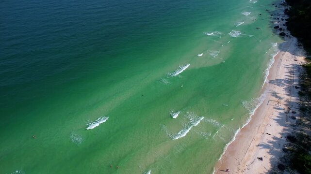 Aerial video of the amazing emerald water white sand Sao Beach with lively water sports, tourists, cabanas and sun umbrellas, beach bar and parasailing. Hot sunny day with long waves on Phu Quoc Islan