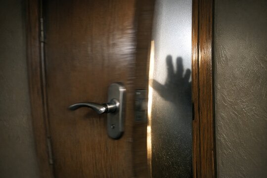 A shadowy hand grasping a door handle