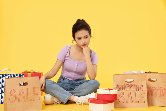 Thoughtful young woman sitting among sale shopping bags