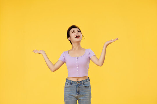Cheerful Young Woman With Open Hands on Yellow Background