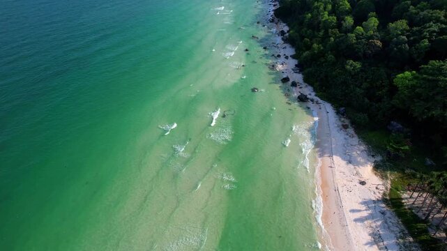 Aerial video of the amazing emerald water white sand Sao Beach with lively water sports, tourists, cabanas and sun umbrellas, beach bar and parasailing. Hot sunny day with long waves on Phu Quoc Islan