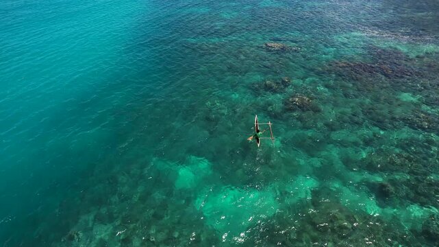 Aerial view of a traditional outrigger canoe floating on crystal clear turquoise water over a vibrant coral reef near Mushu Island, Wewak District, East Sepik Province, Papua New Guinea.