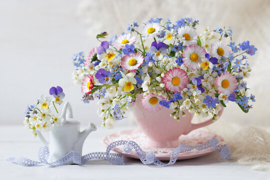 Beautiful spring bouquet of daisies, pansies, forget-me-nots, and bird cherry in a cup and a watering can on the table. Beautiful card.