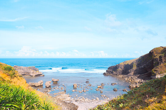 Batanes, Philippines: Dramatic coastal vista of rocky coves and lush green mountains meeting the blue sea under scattered clouds. Nature background.