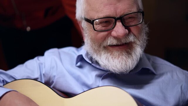 An elderly man playing the guitar, his fingers on the fretboard close up
