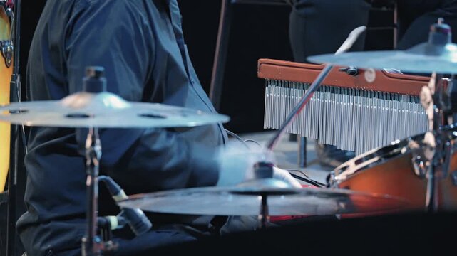 A close-up view of a musician's drum set on stage. The focus is on the metallic chimes cymbals, illuminated by cool stage lighting. Perfect for concepts of live music, jazz festivals, performance